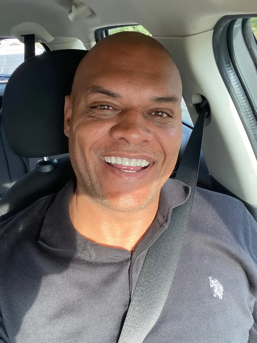 Chris Johnston smiling while sitting in the driver’s seat of his car, capturing a relaxed and confident moment.